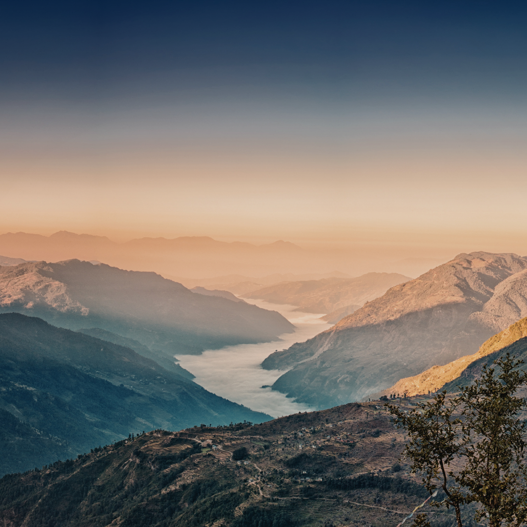 Valley of misty mountains at sunrise with a winding river cutting through the valley and terraced hills in the foreground.
